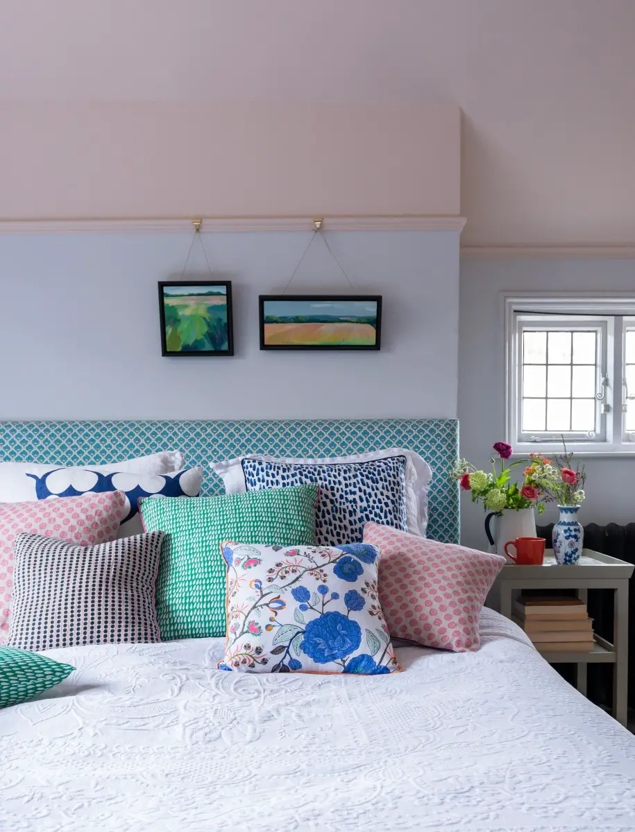colourful cushions piled up on a bed with white bedspread and wooden table