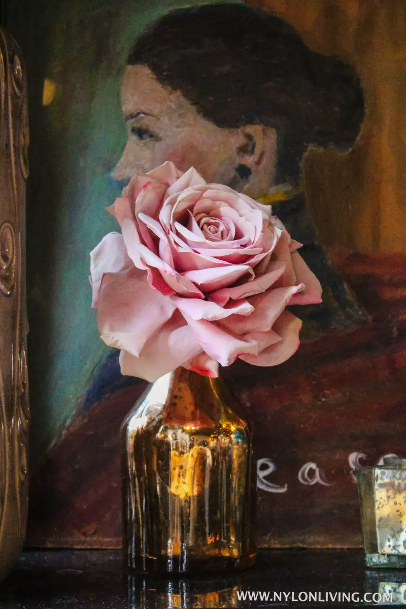 pink rose in a bottle in front of a vintage painting