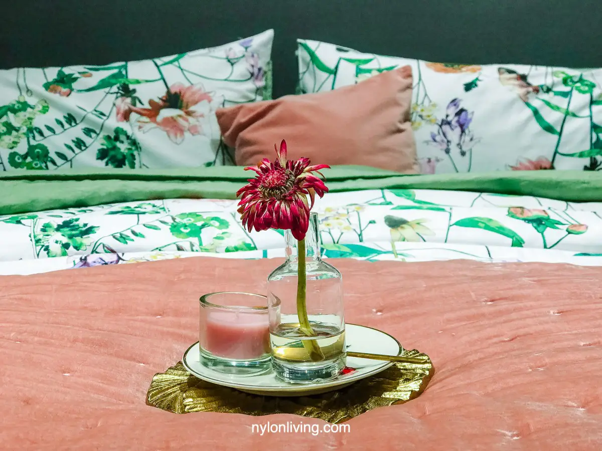 a rose pink pillow with green floral sheets, candle and flower in a vase