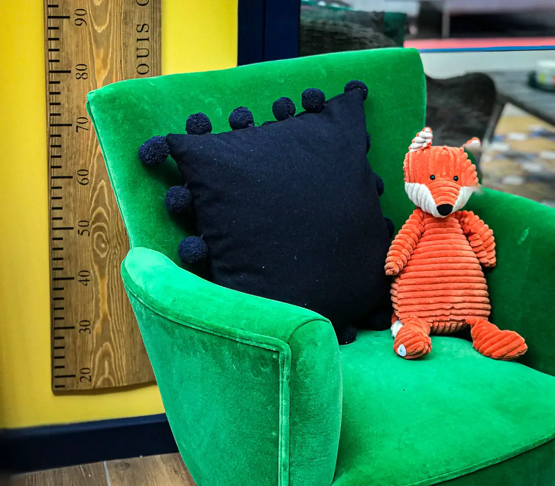 orange fox and a navy pillow on an emerald green velvet chair