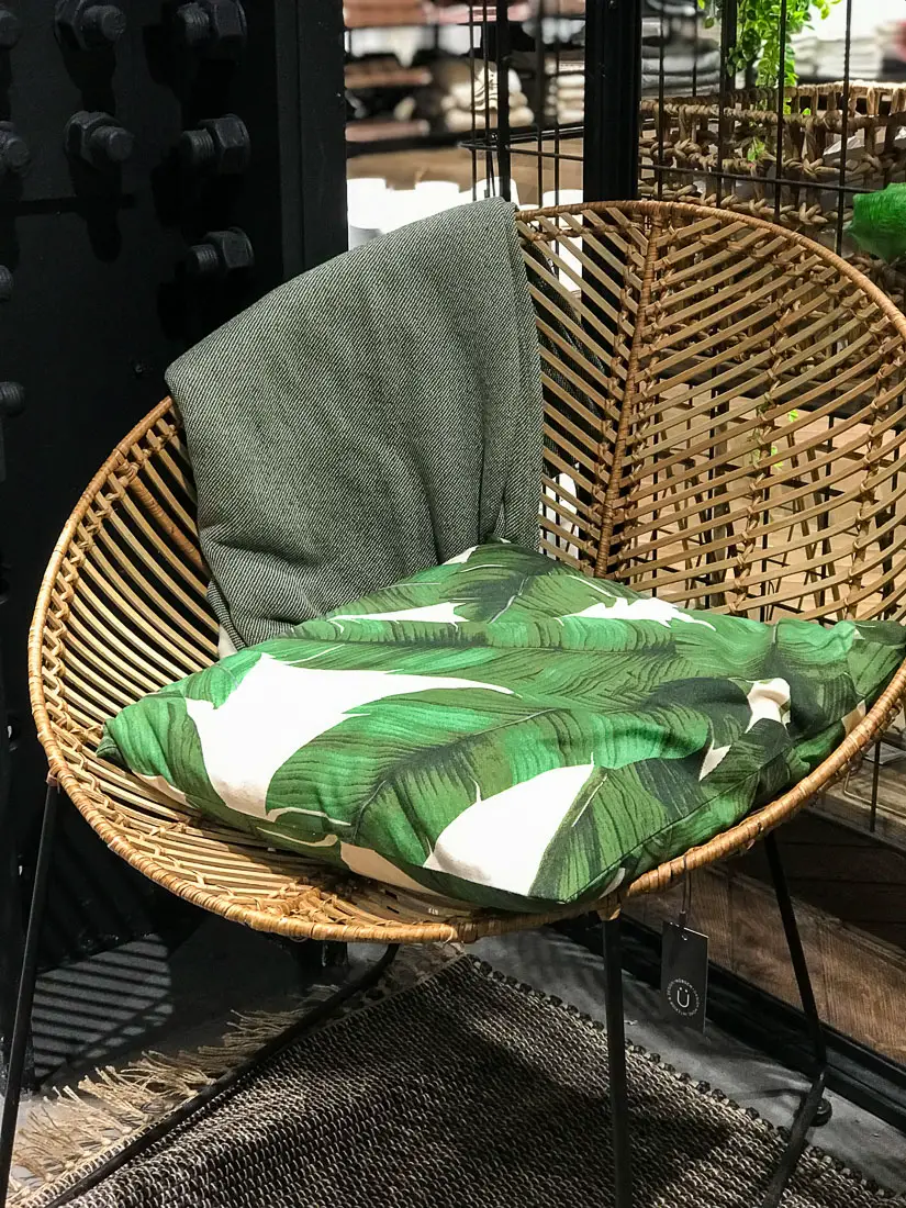 Banana leaf print covered pillow in a modern basket chair.